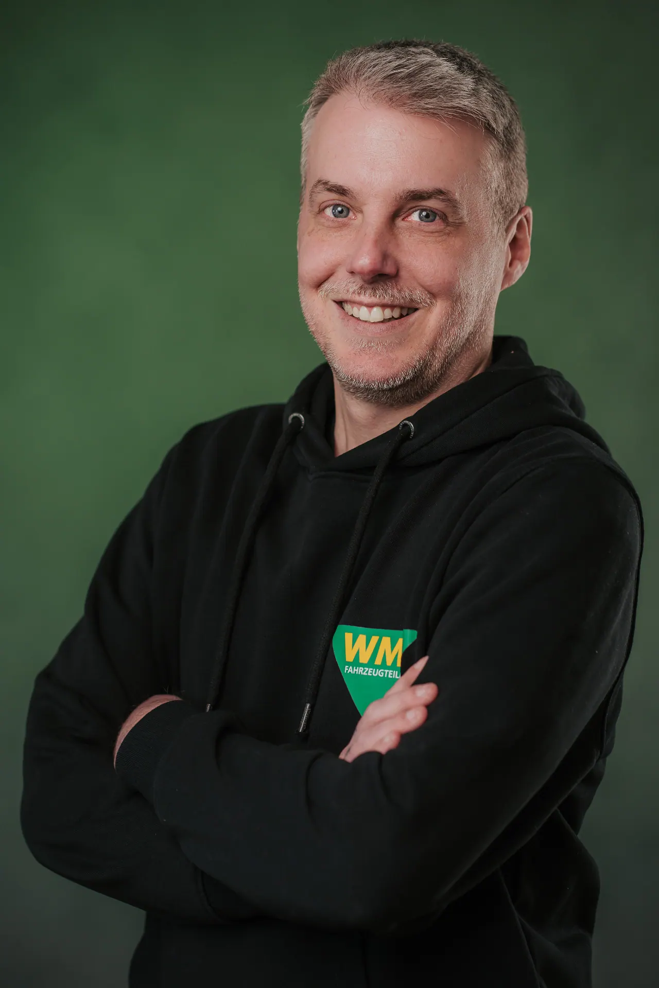 Mitarbeiterportrait — Andreas Greisl vor grünem Studiohintergrund im WM Hoodie