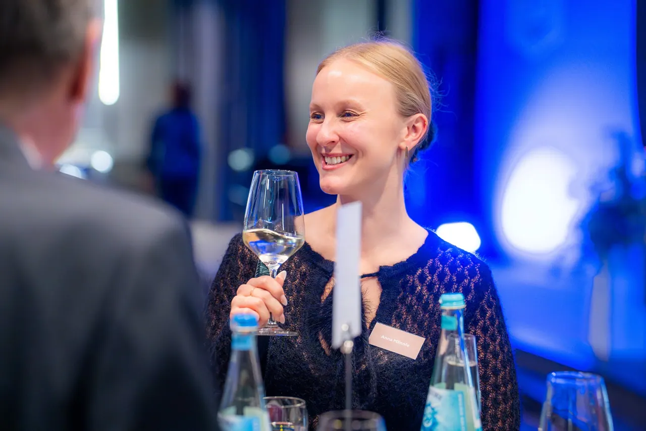 Eventfotografie — Lächelnde Gästin mit Weißweinglas im Gespräch
