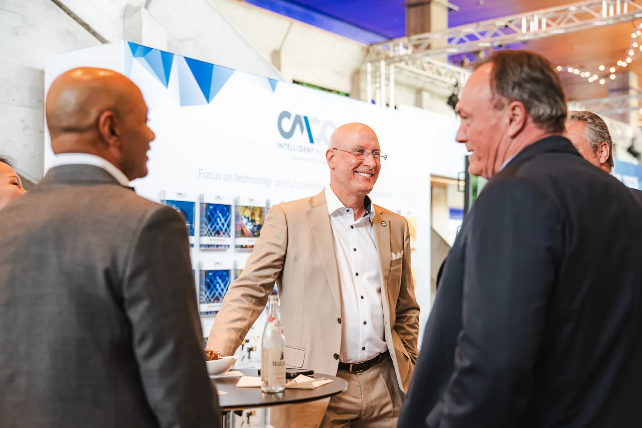 CMCO Customer Exchange & Show 2025 — Networking am Stehtisch vor CMCO-Branding-Wand