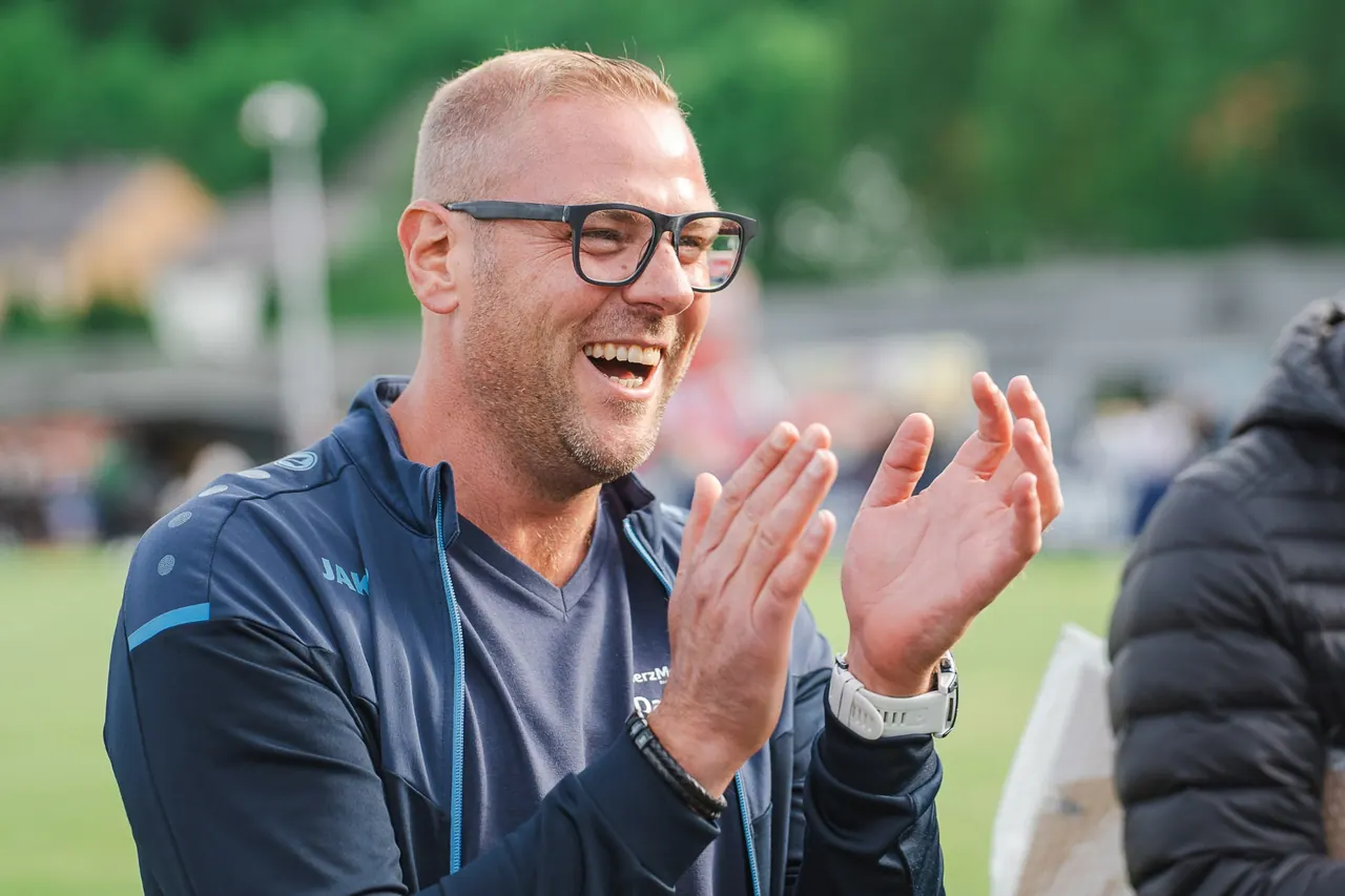 R+V Herzmomente 2025 — Lachender klatschender Gast in JAKO-Trainingsjacke am Spielfeldrand