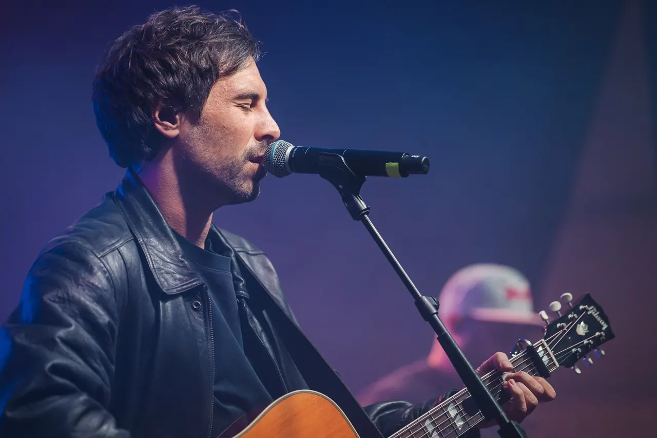 R+V Herzmomente 2025 — Max Giesinger singt mit Akustikgitarre im violetten Bühnenlicht